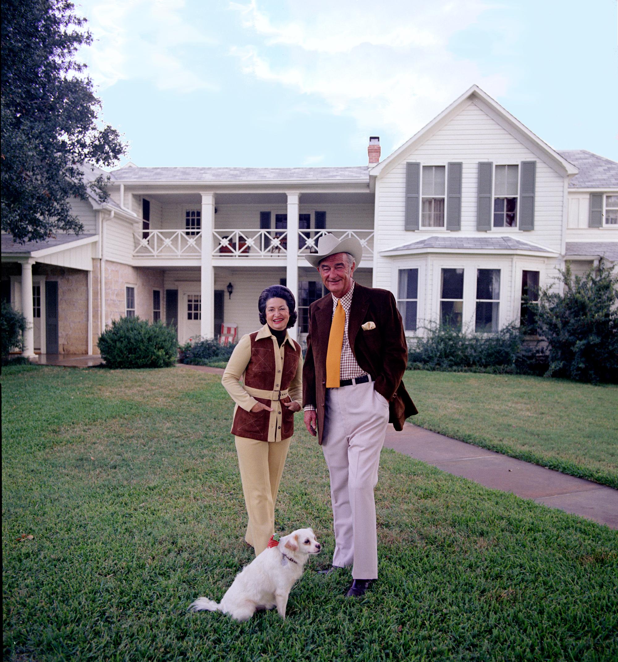 President and Mrs. Johnson stand with their small, white dog in front of the Texas White House.