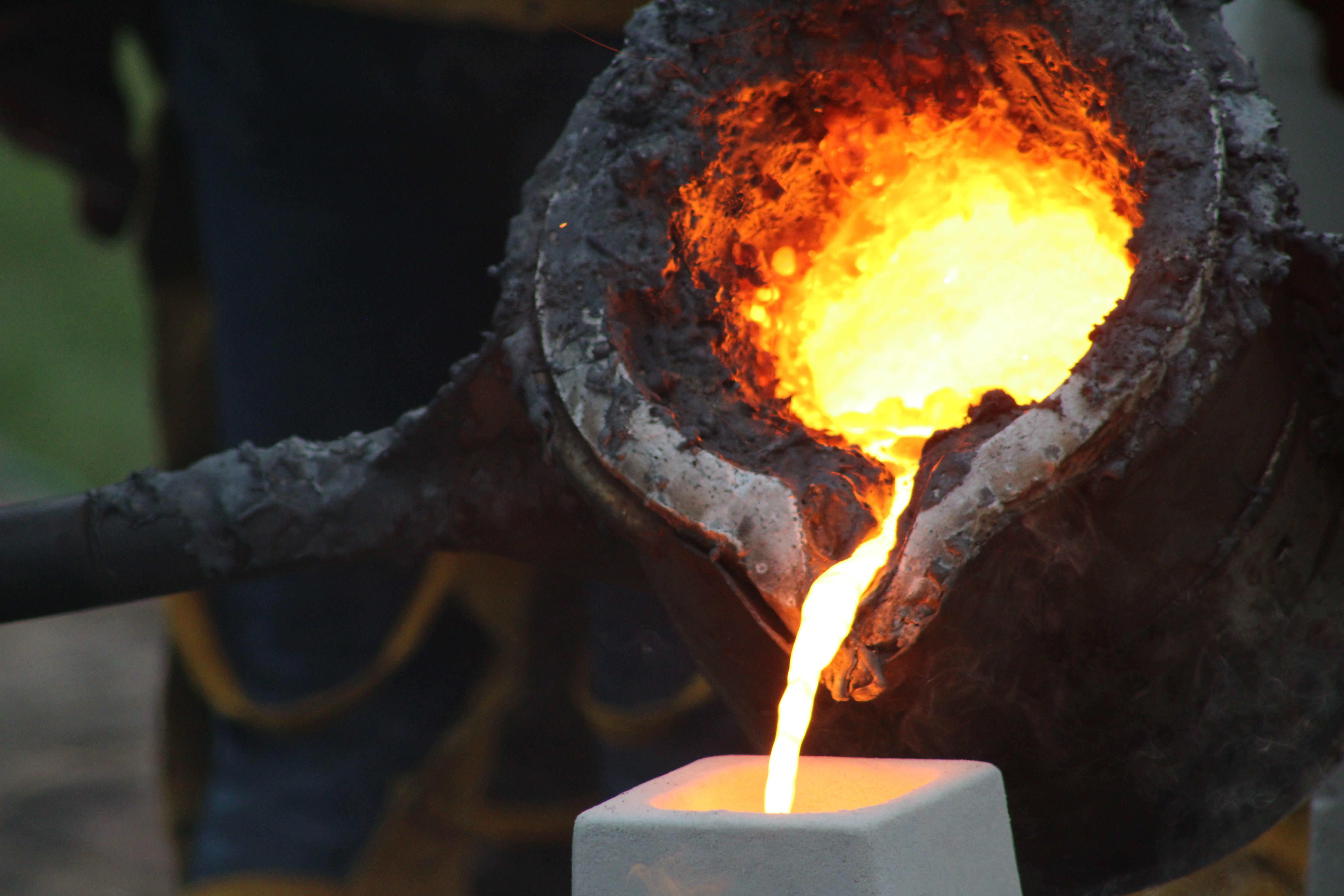Melted iron pouring into a mold from a metal bucket.