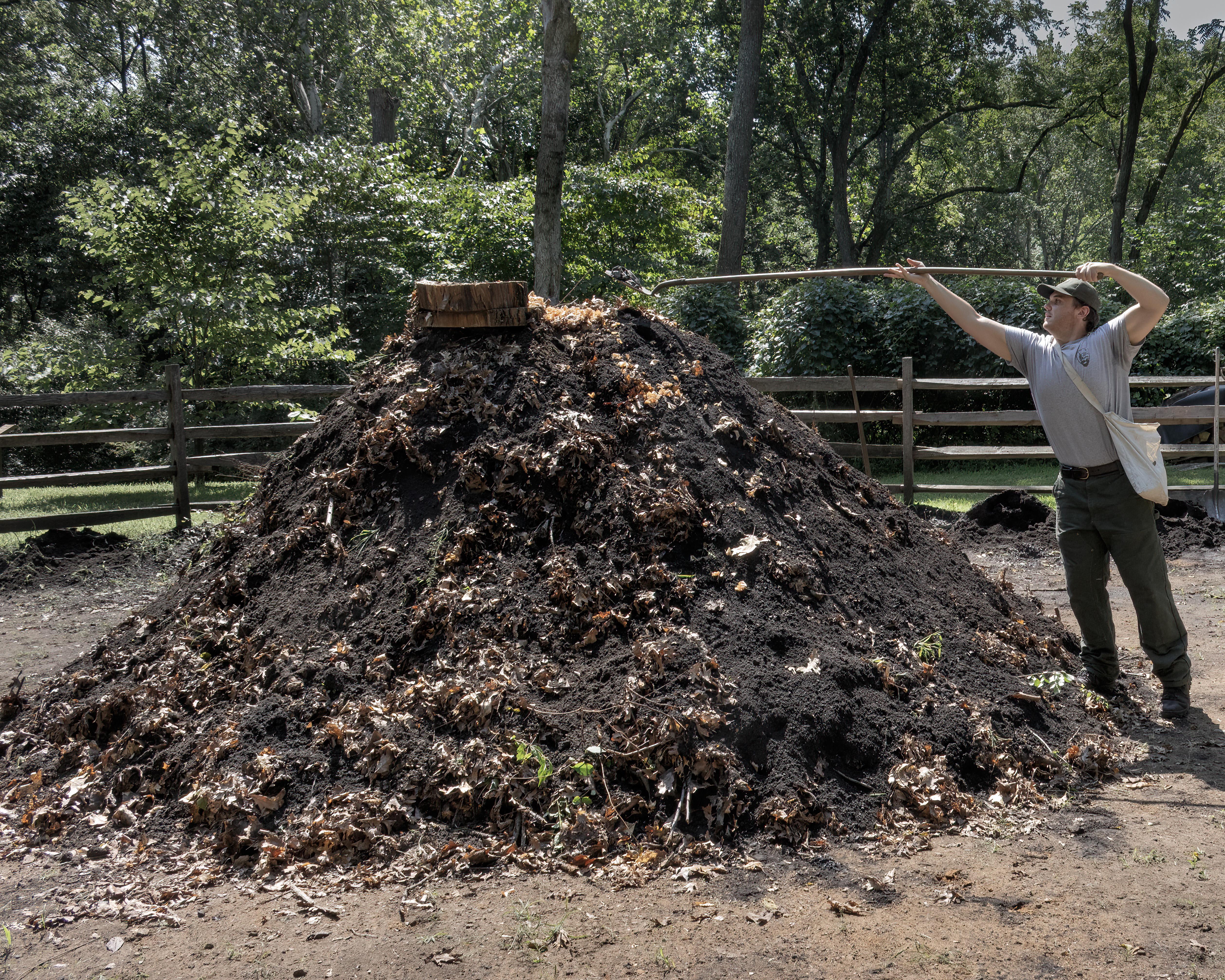 a large dirt pile with smoke coming out of the top. A park ranger scopes more dirt with a shovel.