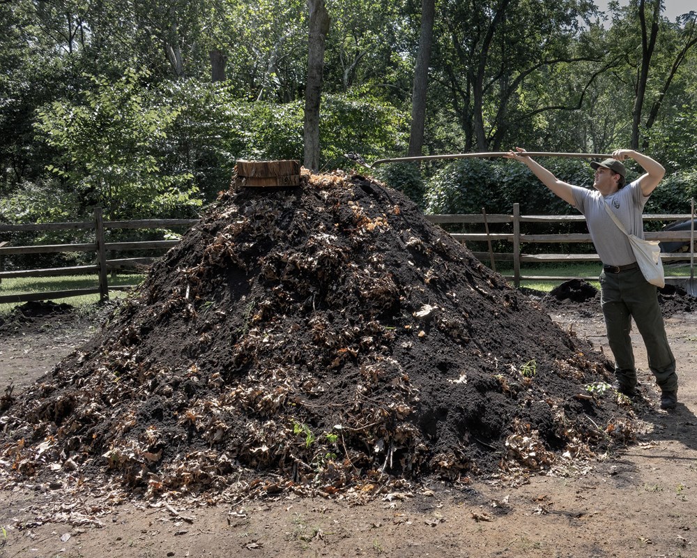 a large dirt pile with smoke coming out of the top. A park ranger scopes more dirt with a shovel. 