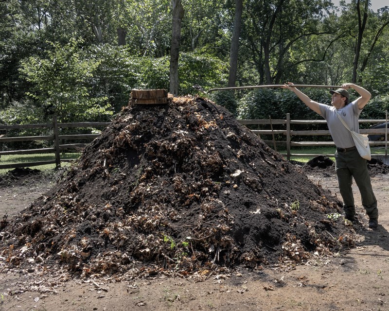 a large dirt pile with smoke coming out of the top. A park ranger scopes more dirt with a shovel.