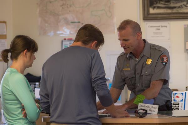 A ranger talking with two visitors at a desk in a visitor center