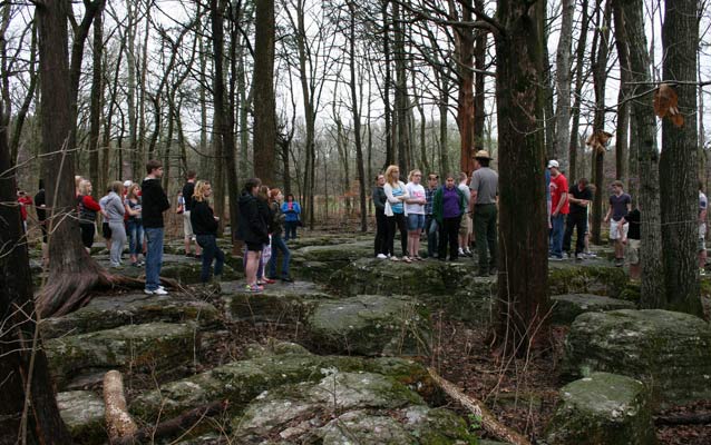 Students stand among rocky outcroppings listening to a park ranger.