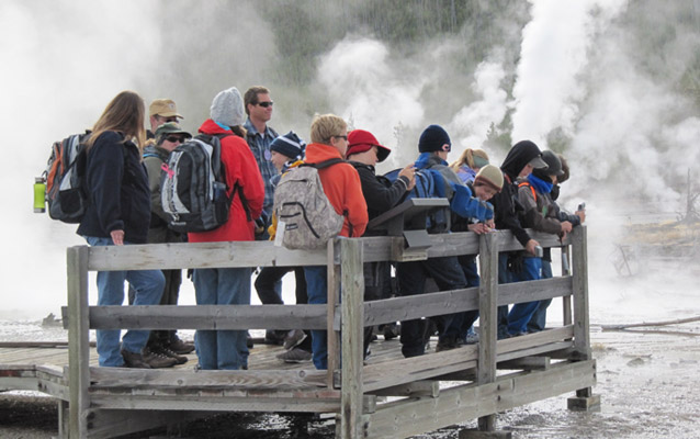 A school group and ranger near a thermal feature with steam in background