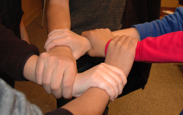 Five interlocking hands grabbing the wrist of the person next to them