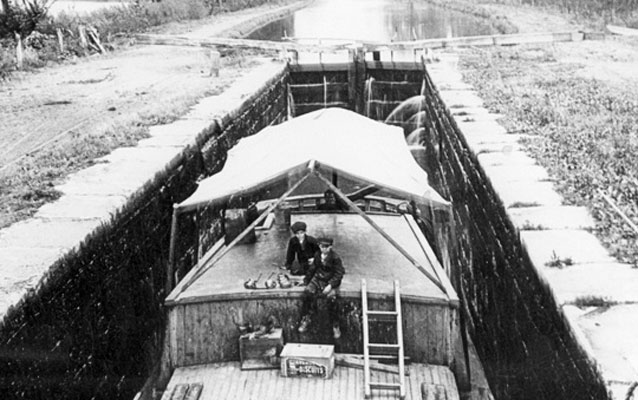 An historic black and white photo of two boys on a canal boat in a lock. An historic black and white photo of two boys on a canal boat in a lock.
