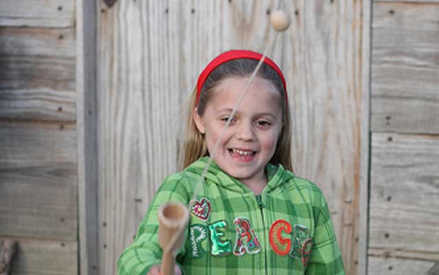 A girl standing in front of wooden barracks plays with a cup and ball toy.