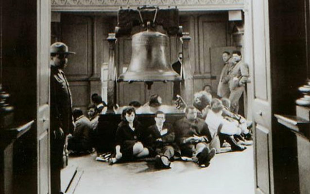 Black and white photo showing students sitting around the base of the platform supporting the Liberty Bell. Black and white photo showing students sitting around the base of the platform supporting the Liberty Bell.
