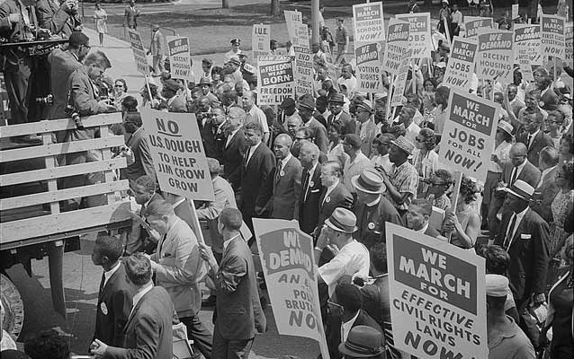 Black and white photo from the 1960's showing a large crowd walking forward and holding signs about civil rights. Black and white photo from the 1960's showing a large crowd walking forward and holding signs about civil rights.