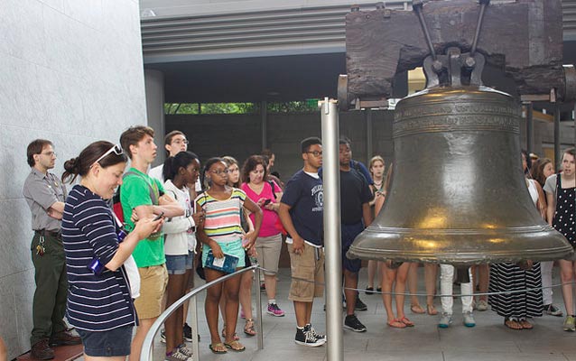Color photo of a group of teens looking at the Liberty Bell while a male park ranger stands off to the side. Color photo of a group of teens looking at the Liberty Bell while a male park ranger stands off to the side.
