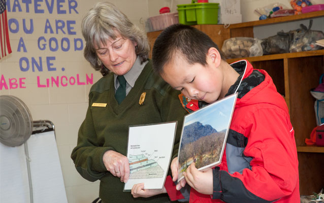 A park ranger holds up a photo while a child holds up another picture beside her. A park ranger holds up a photo while a child holds up another picture beside her.