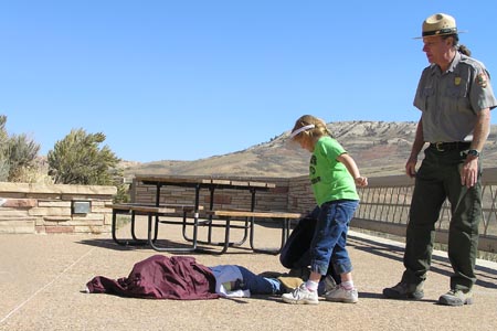 Student burying student-fish with coat while a ranger oversees it