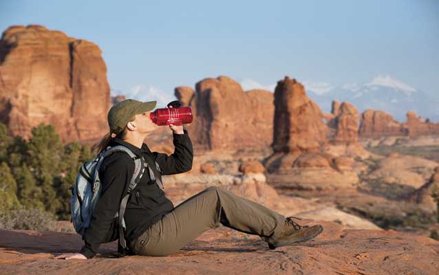 a woman drinks from a red water bottle