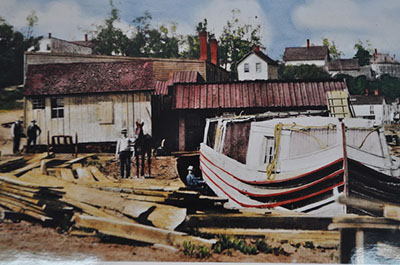 A colorized photo of a canal boat, lumber and workers in a boatyard along the Ohio and Erie Canal