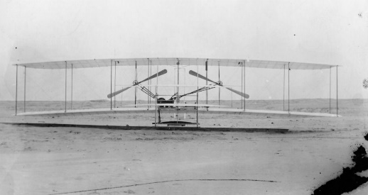 black and white photo of a bi-wing plane sitting on a stretch of sand