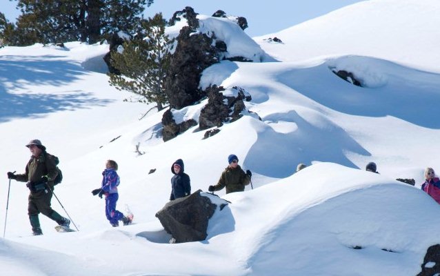 snowshoers follow a  ranger across a rocky landscape covered in snow