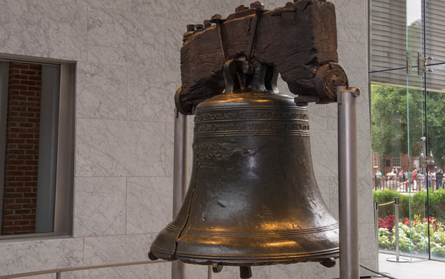 Color photo of the Liberty Bell shown from the side, with the brown wooden yoke resting on two steel supports