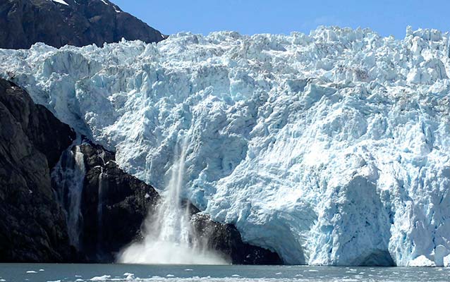 Enormous tidewater glacier, with a piece of glacier calving, or falling, into the ocean.