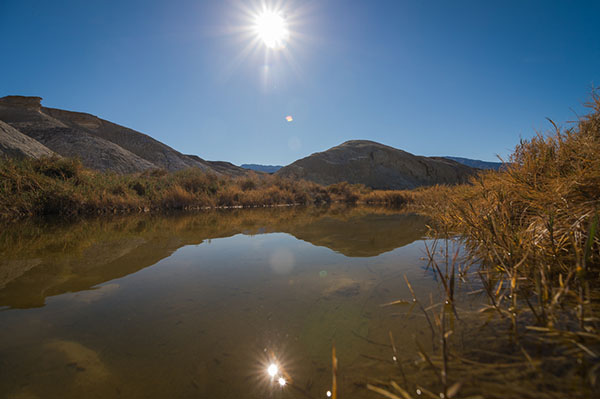 The sun shines above a pool of water surrounded by hills.