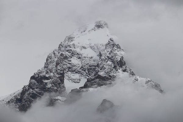 A rocky mountain peak peeking out of the clouds and covered in a fresh coat of snow