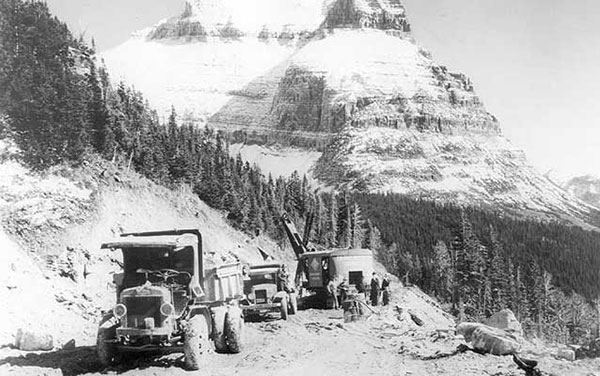 a historic photo with large vehicles in the foreground and mountains in the background. 