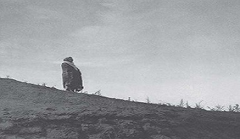 Adult covered in a blanket stands on a dirt hill looking to the right. Adult covered in a blanket stands on a dirt hill looking to the right.