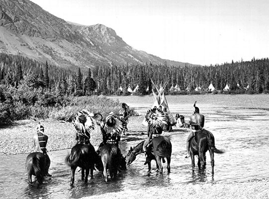 five horses with riders stand in a river in this historic photo