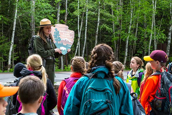 Ranger holding an NPS arrowhead and young students. Ranger holding an NPS arrowhead and young students.
