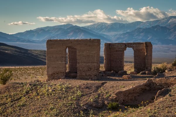 The ruins of an old building that has only two walls still standing with mountains in the background.