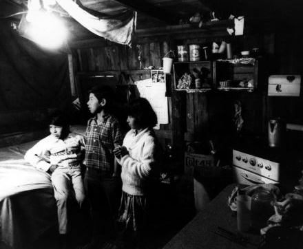Three children stand in a shanty home typical of California farmworkers in the 1970s. Image-Wayne State University Three children stand in a shanty home typical of California farmworkers in the 1970s. Image-Wayne State University