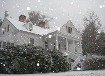 The white historic home of Carl Sandburg sits on a hill as snow drifts down covering the ground.
