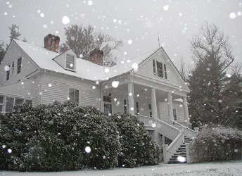 The white historic home of Carl Sandburg sits on a hill as snow drifts down covering the ground. The white historic home of Carl Sandburg sits on a hill as snow drifts down covering the ground.