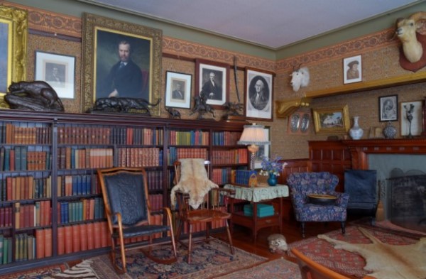 A interior view of Theodore Roosevelt's library with chairs, books, hunting trophies, and portraits.