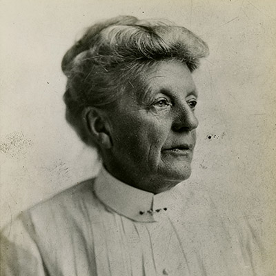Black and white portrait of an older woman wearing a light-colored, pleated blouse with a straight, decorative pin at the collar.