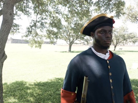 Reenactor in Fort Mose Military uniform holding a musket with Castillo in the background. Reenactor in Fort Mose Military uniform holding a musket with Castillo in the background.