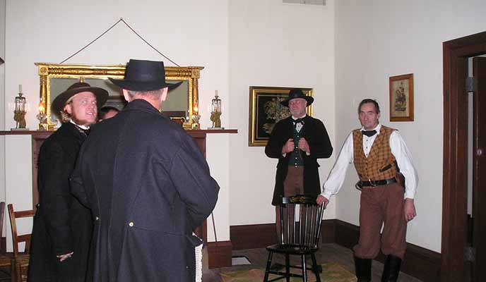Four men weaing historical clothes stand facing each other in a room. Four men weaing historical clothes stand facing each other in a room.