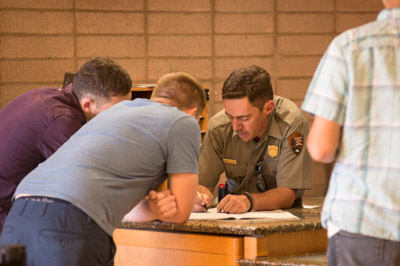 A park ranger plans a trip with two visitors at a desk. A park ranger plans a trip with two visitors at a desk.