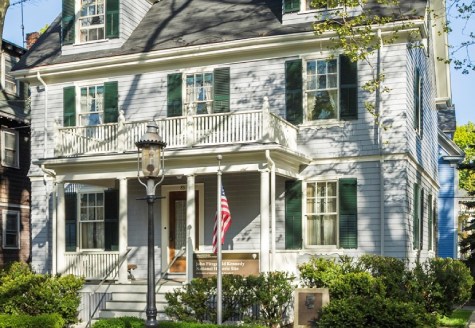 A three story house with a lamppost, American flag, National Park Site sign, and plaque bearing JFK's likeness in front. A three story house with a lamppost, American flag, National Park Site sign, and plaque bearing JFK's likeness in front.