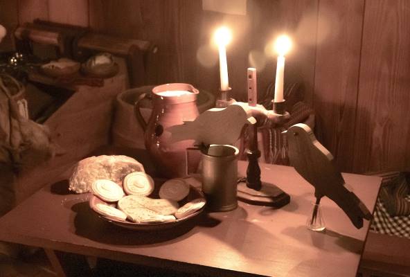 A candlelit table with a plate of cookies, jar of milk, and two wooden birds arranged carefully on it. 