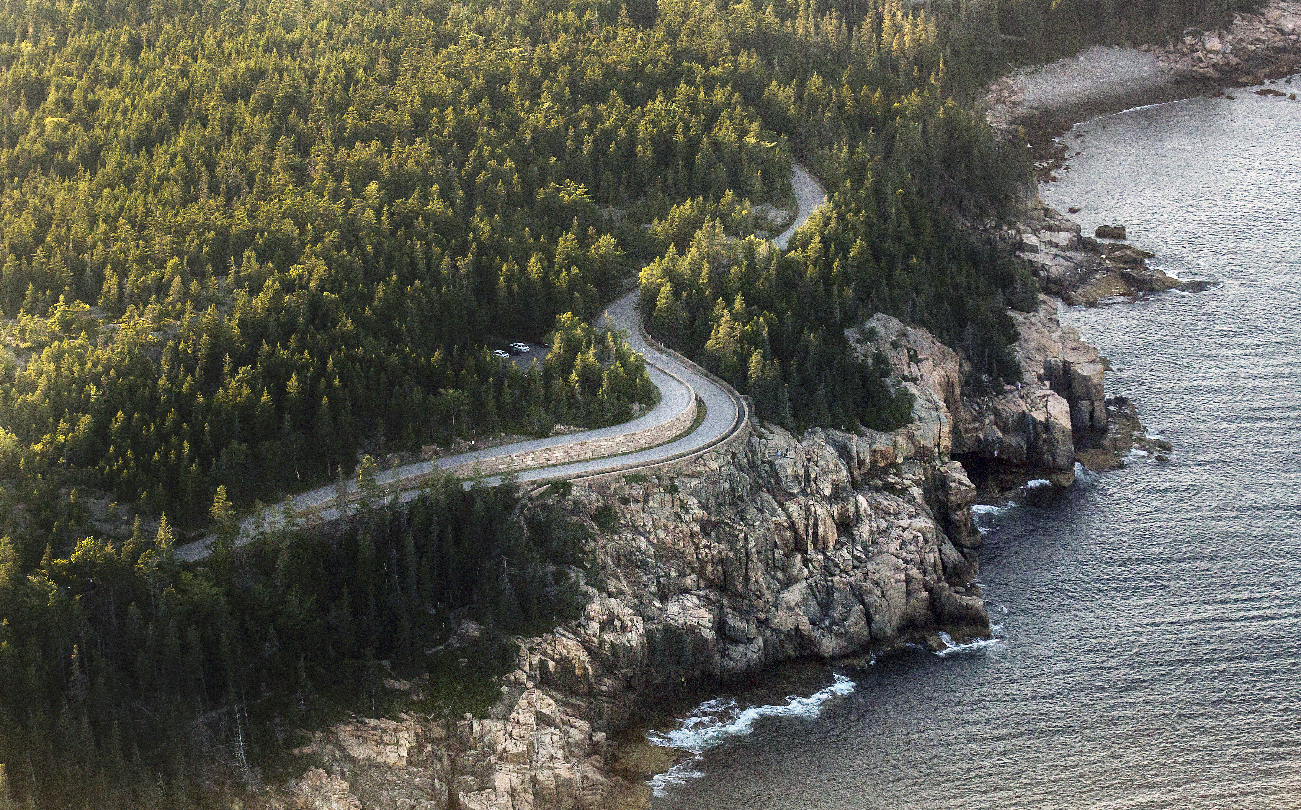 Park loop road viewed from a bird's eye view, curving through trees next to a rock cliff side.