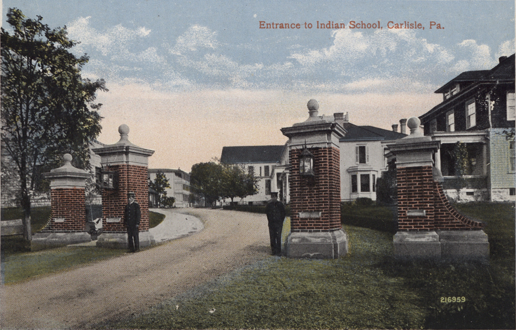 Two soldiers stand guard in front of brick gateposts that rise at least twice the size of a man.