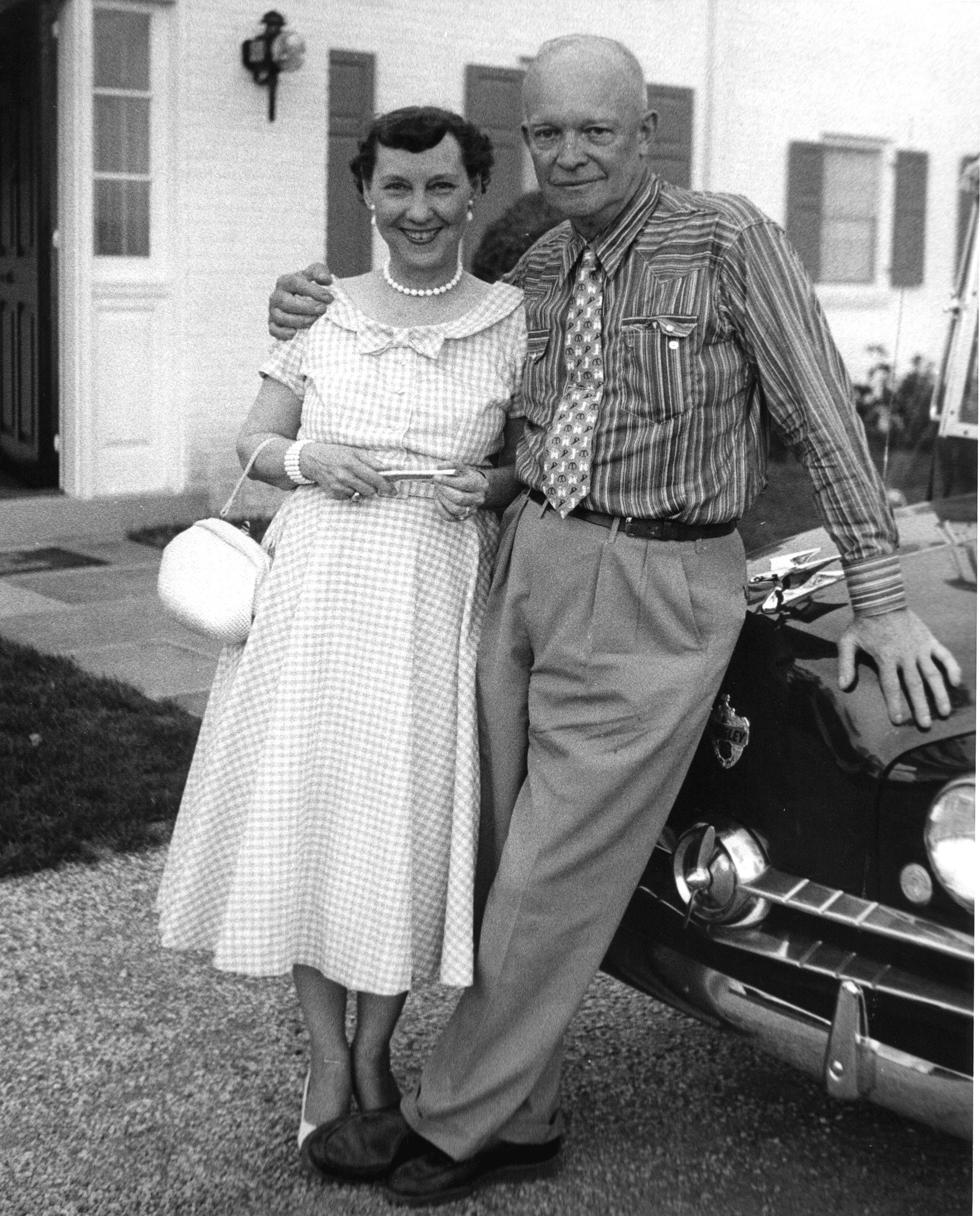 Mamie Eisenhower stands next to the General who has his arm around her shoulders.