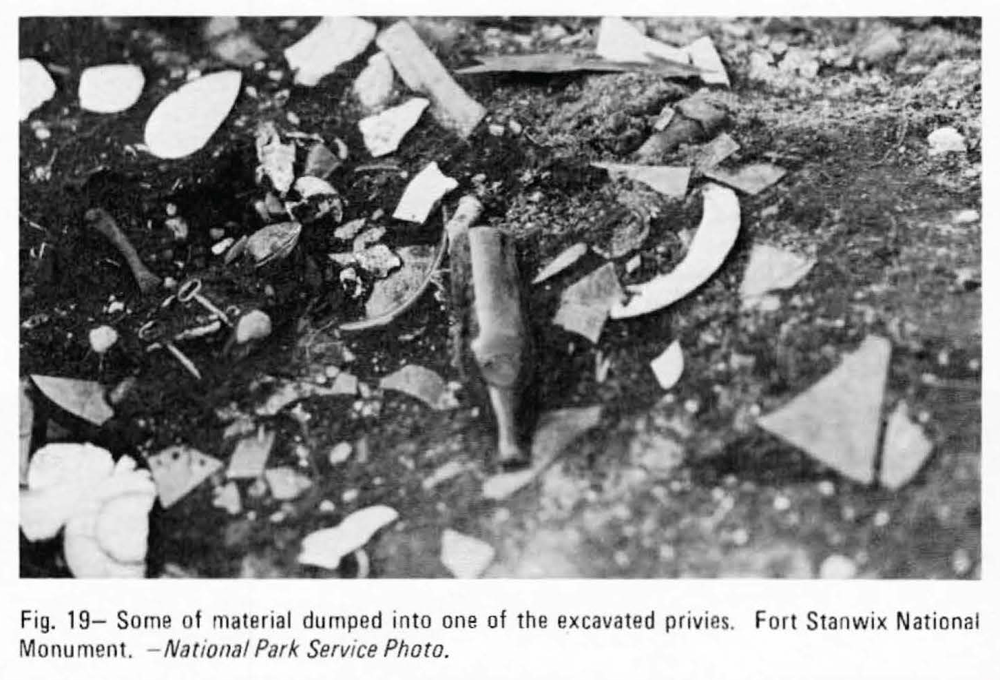 A gravel-filled pit with broken bottles, pottery sherds, and skeleton keys strewn in it.
