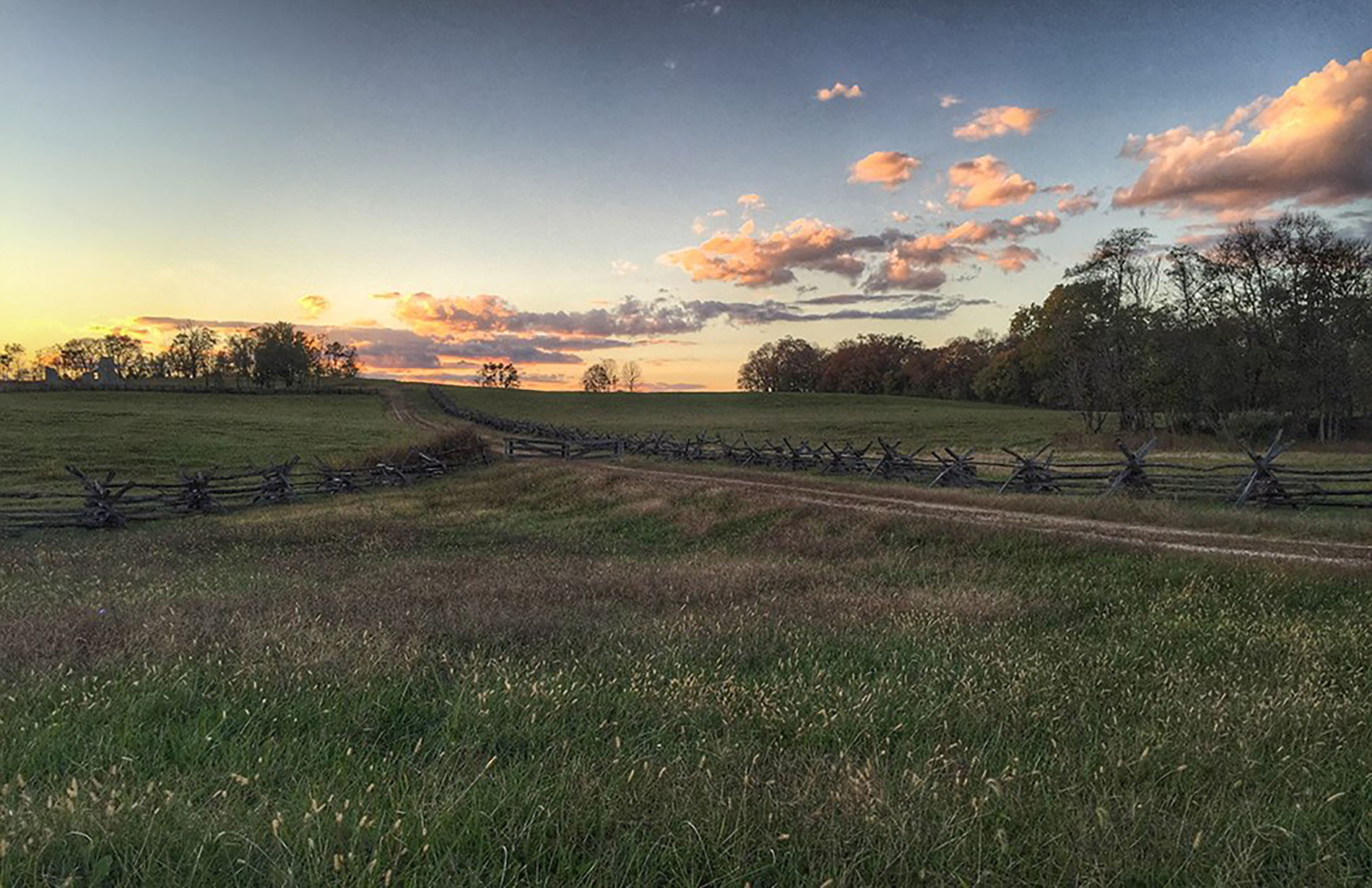 Split-rail fencing runs along a dirt road through a grassy field