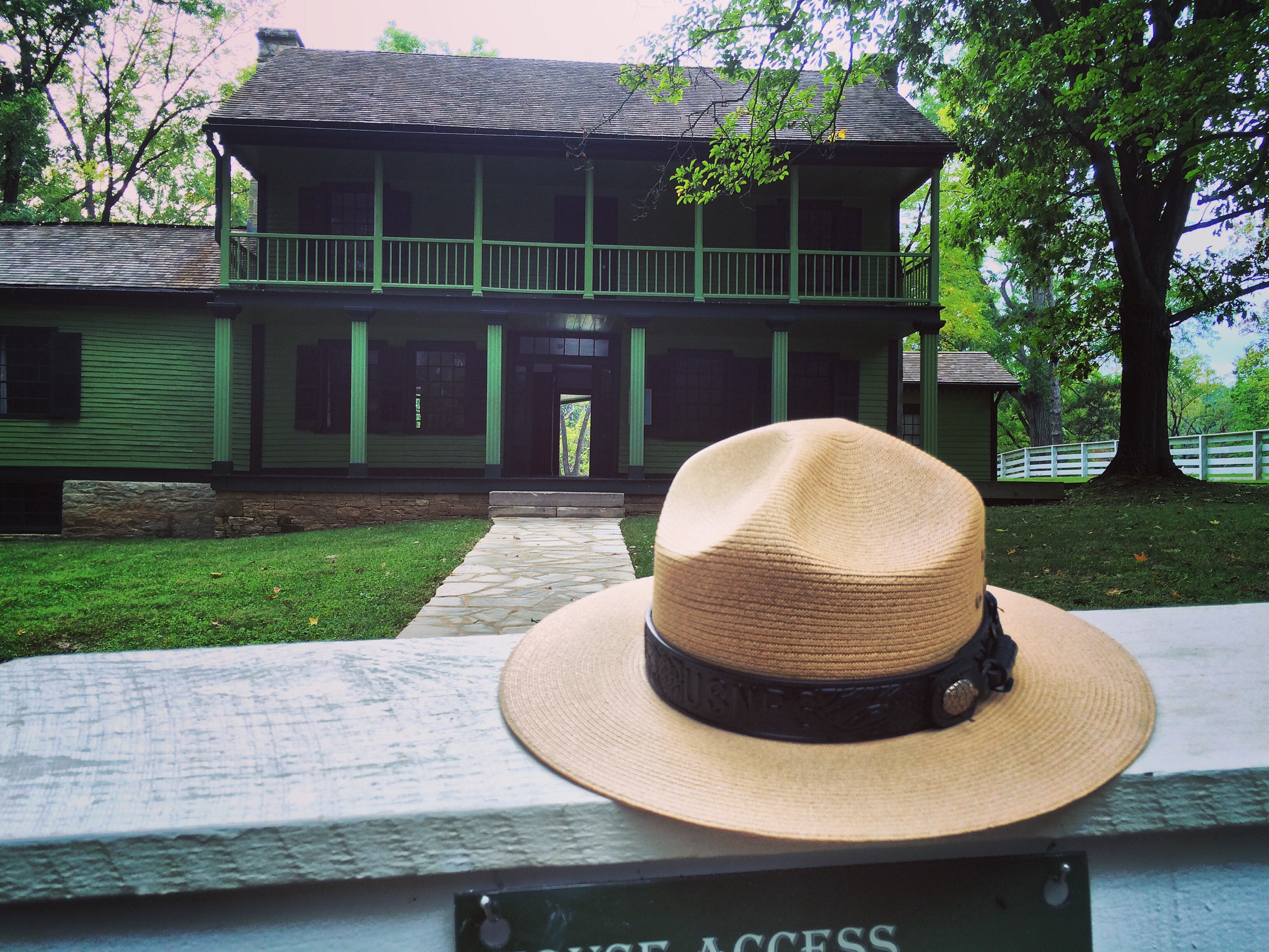 A tan ranger hat sits on a white fence. In the background is a two story green house.