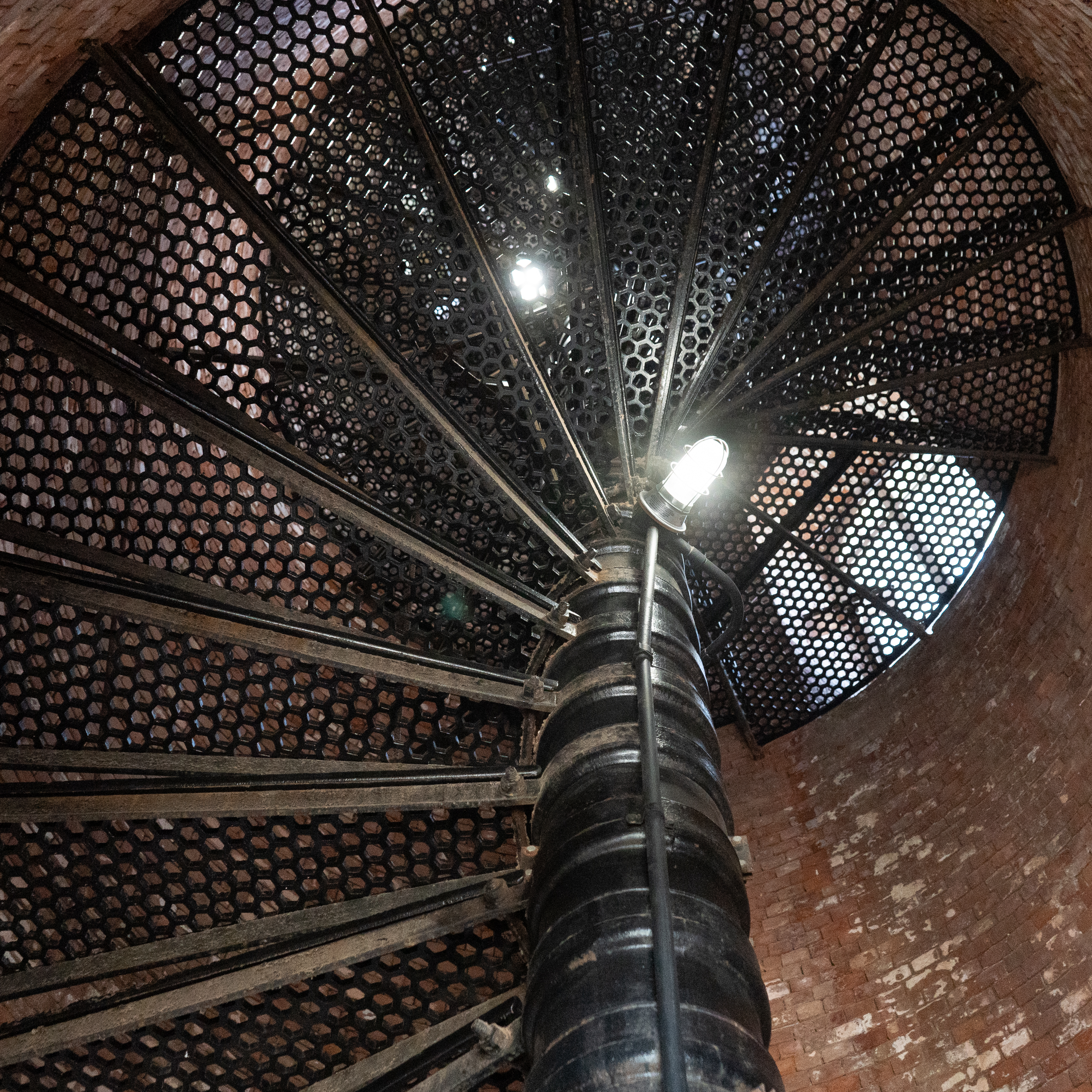 A metal spiral staircase with brick walls surrounding.