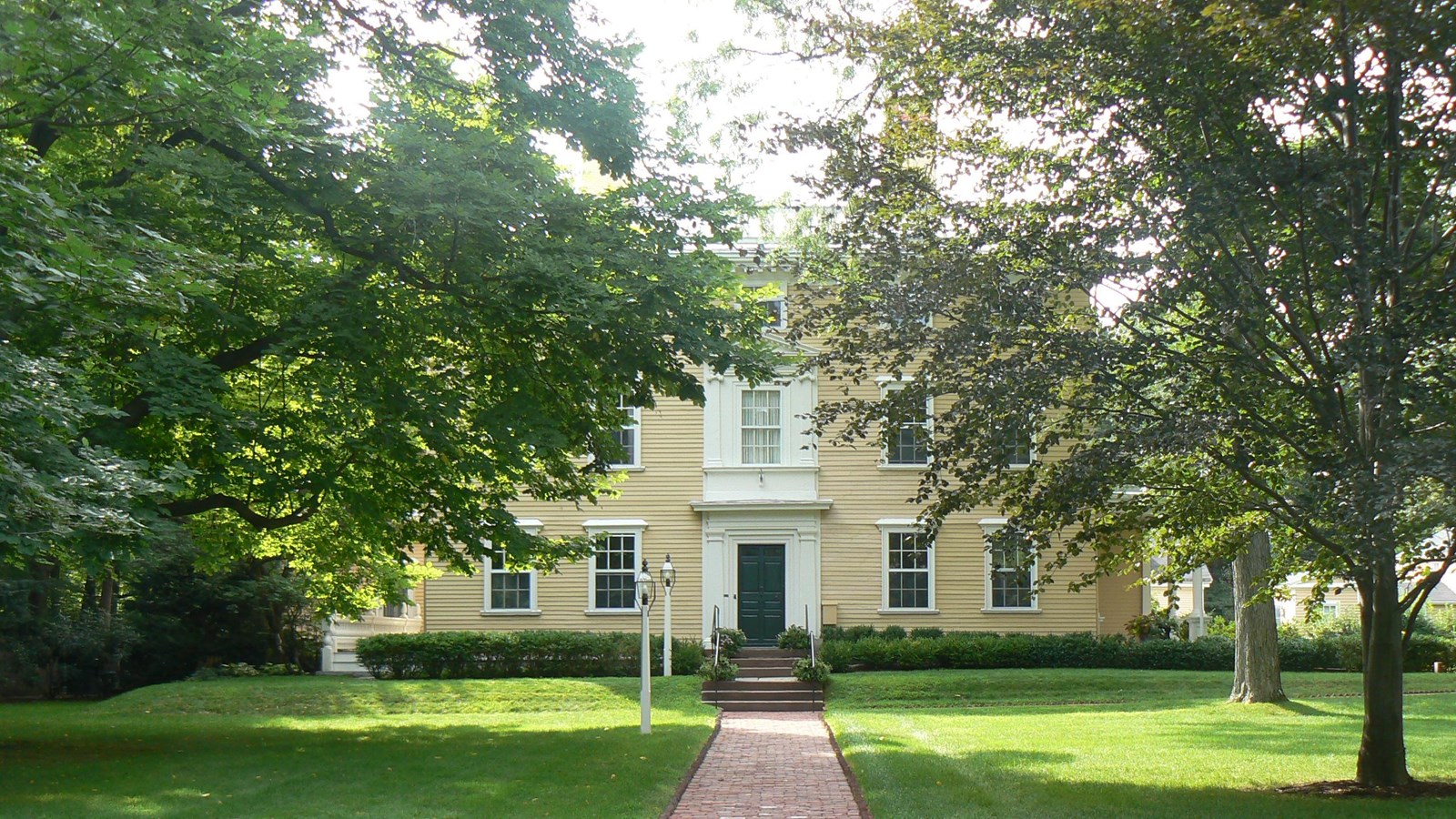 alt="Large symmetrical Georgian house partially obscured by large trees"
