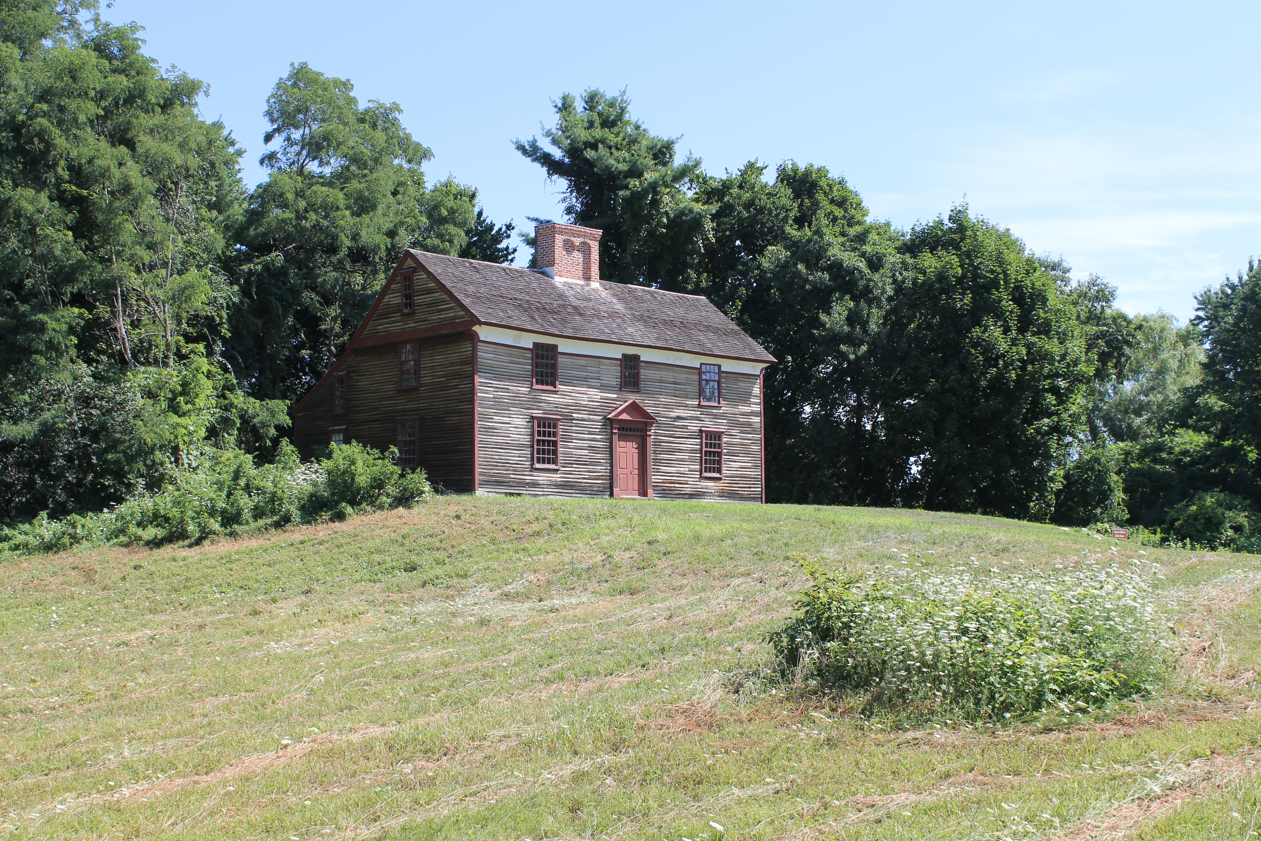 Two story wooden colonial house on a grassy hill.