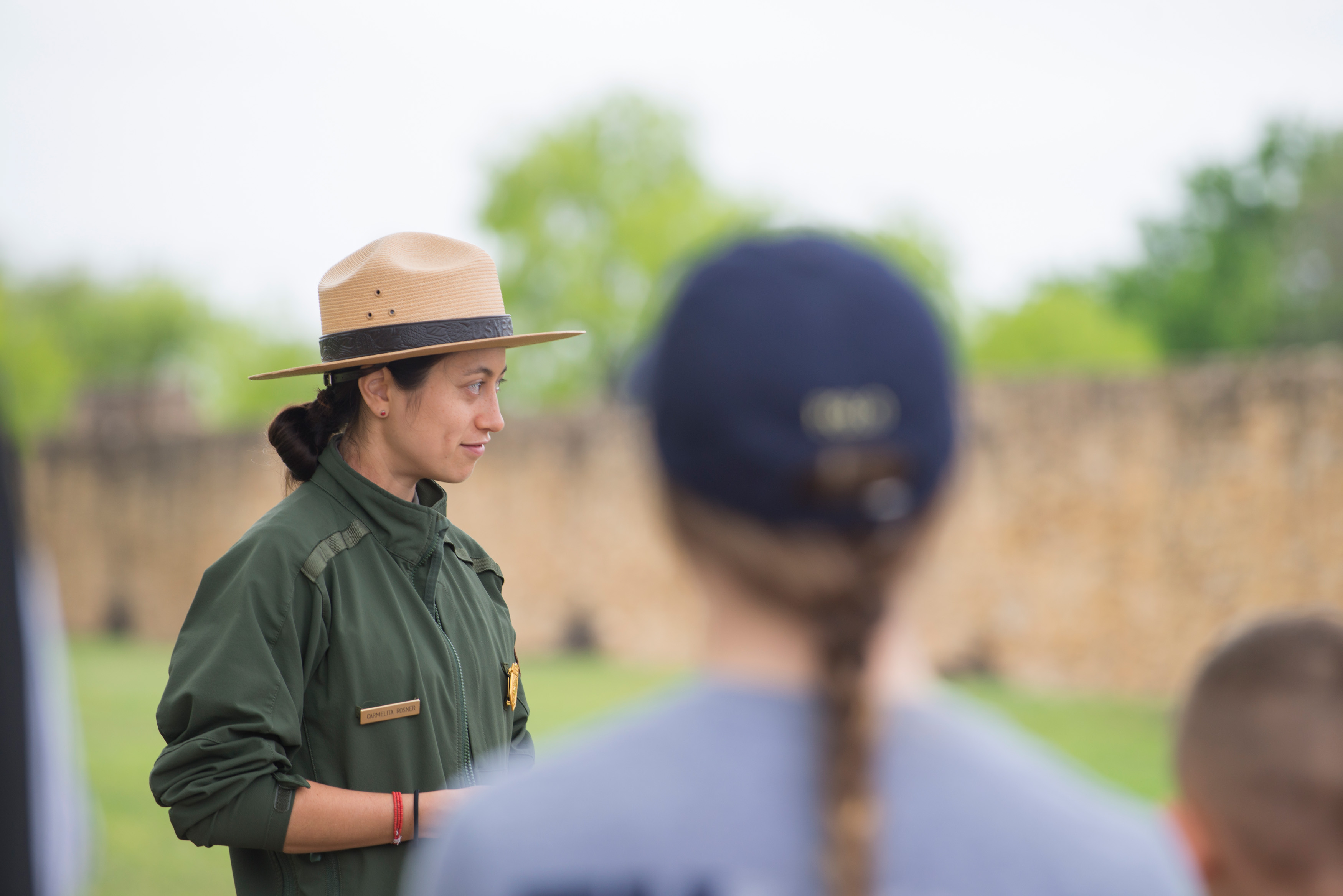 Park Ranger stands in front if visitors with Mission San Jose limestone walls in background.