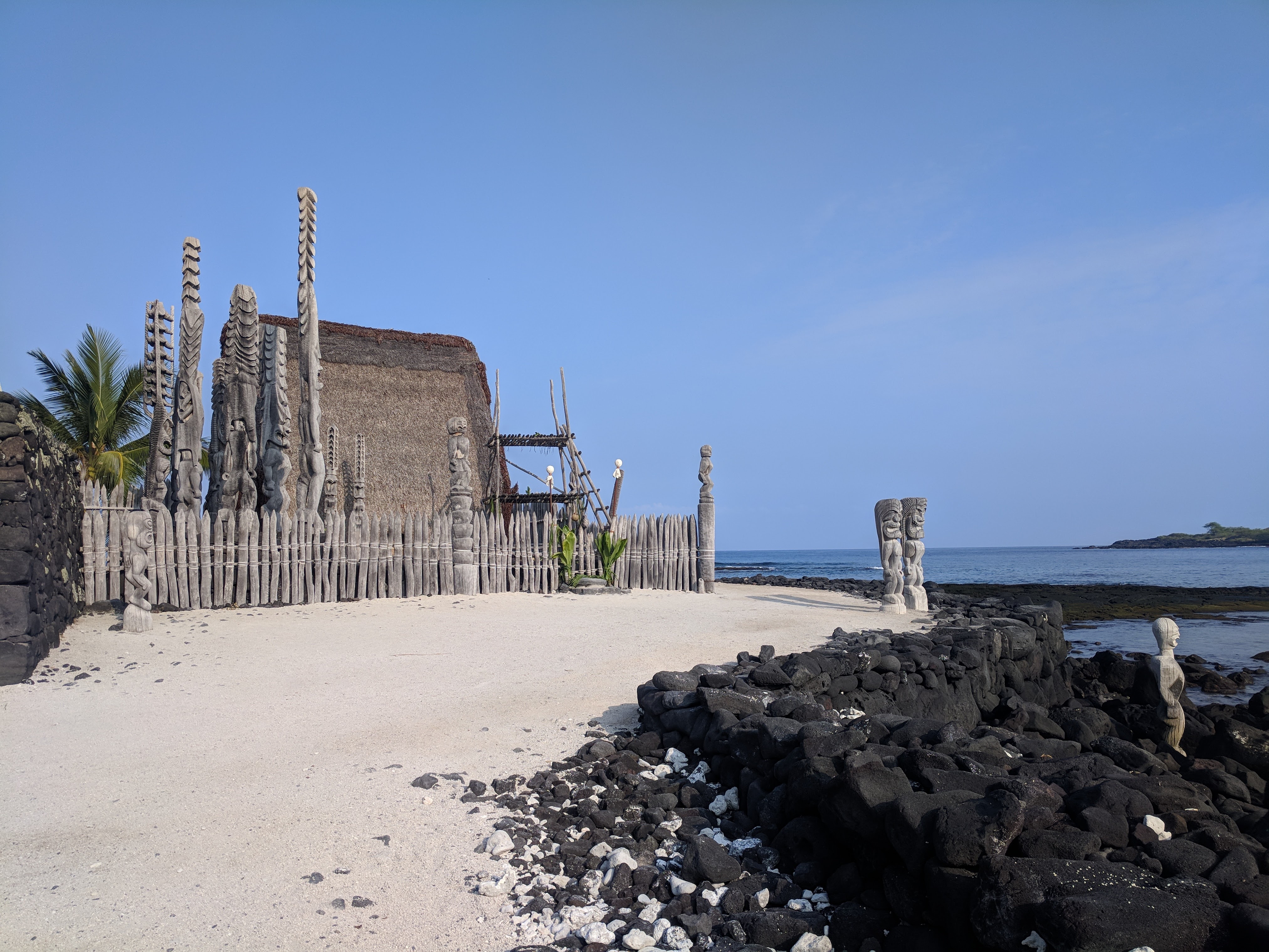 Thatched Hale o Keawe with accompanying carved kiʻi images, offering platform, and wooden palisade